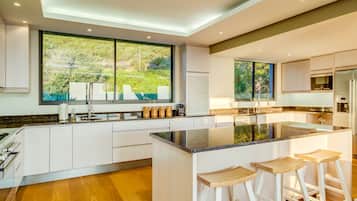 A modern kitchen with a large island, white cabinetry, and a view of greenery outside.