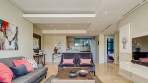 A modern living room with a sofa, coffee table, and a dining area. - 308 Juliette on the Waterfront Marina (Cape Town)