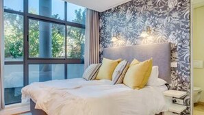 A bedroom with a large window, a bed with white bedding, and a nightstand with a lamp. - 308 Juliette on the Waterfront Marina (Cape Town)