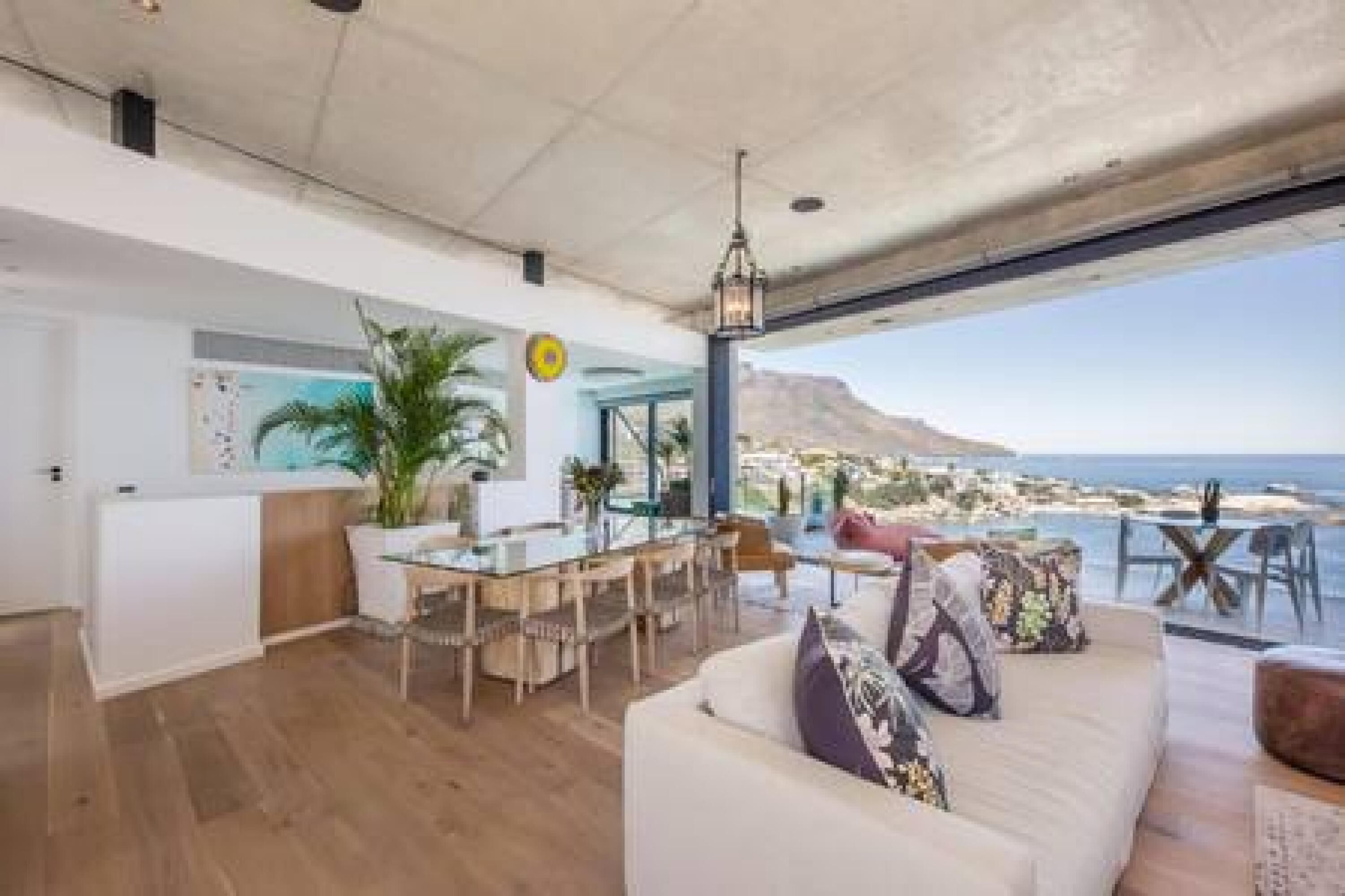 A spacious living area with a large window overlooking a coastal view, a dining area with a glass table, and a modern kitchen.