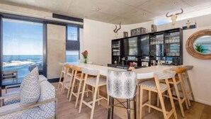 A modern kitchen with a bar area, large windows, and a view of the sea. - Spectacular Ocean Villa in Camps Bay (Cape Town)