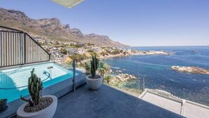 A balcony with a pool, overlooking a coastal town and mountains. - Spectacular Ocean Villa in Camps Bay (Cape Town)