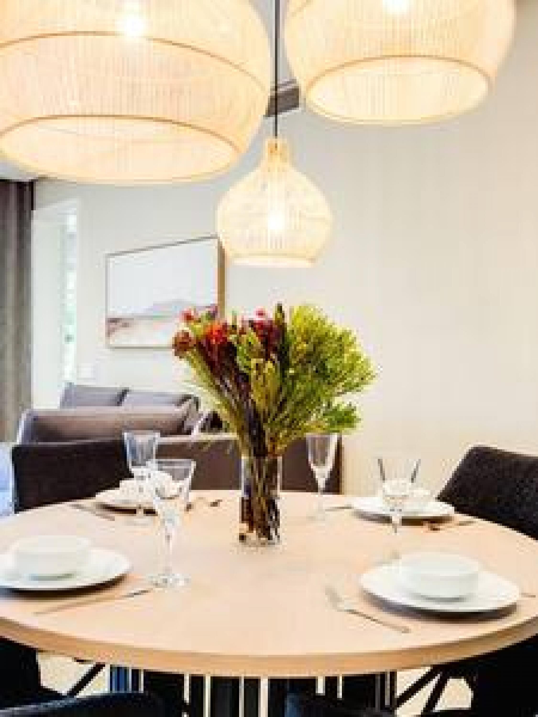 A round dining table with white plates, glasses, and a vase with flowers.