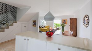 A modern kitchen with white cabinetry, a light countertop, and a hanging pendant light. There is a red fruit bowl on the counter and a yellow sofa in the background. - Unique City View Apartment in De Waterkant 207 DWP (Cape Town)