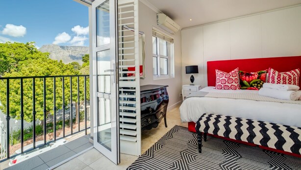 Une chambre avec une grande fenêtre, un lit doté d’une tête de lit rouge et une vue sur la verdure à l’extérieur.