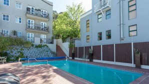 Une piscine entourée d’une terrasse en briques, elle-même bordée d’un bâtiment doté de balcons et d’un escalier menant à un niveau supérieur.