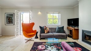 Un salon moderne avec un canapé, un fauteuil orange, une table basse en verre et une cheminée.