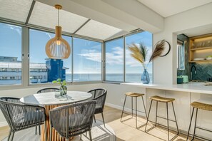 A modern kitchen with a white countertop, bar stools, and a view of the ocean. - Exquisite Mouille Point Apt by Golf Course Serene Suite (Cape Town)