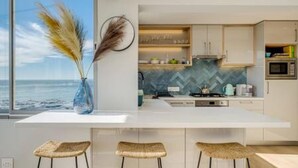 Cozinha moderna com ilha grande, armários brancos e vista para o oceano.