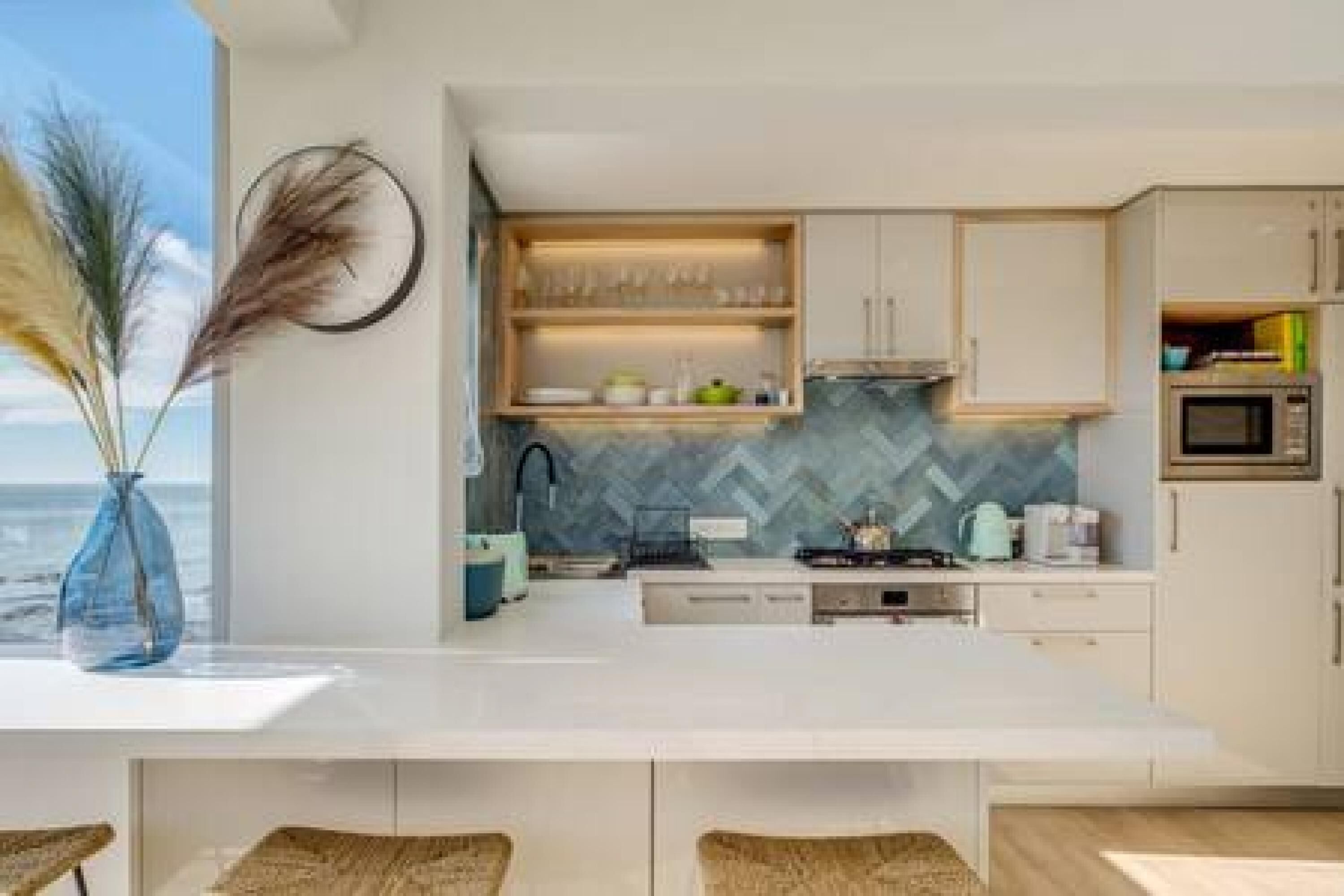 A modern kitchen with white cabinets, a herringbone backsplash, and a view of the ocean.