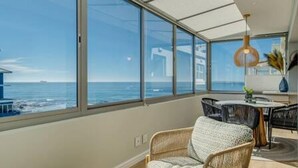 Quarto moderno com amplas janelas com vista para o mar, uma mesa de jantar redonda e móveis de vime.