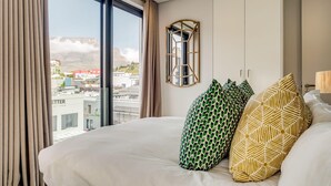 Ein Hotelzimmer mit einem großen Bett, Blick auf eine Stadtlandschaft und einem Spiegel an der Wand.
