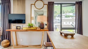 Ein modernes Wohnzimmer mit Couchtisch aus Holz, einem an der Wand montierten Fernseher und einem großen Fenster mit Vorhängen.