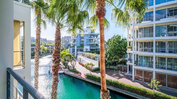 A modern building with balconies overlooking a water feature and greenery. - Modern Waterfront Apartment w Canal Views Gulmarn 201 (Cape Town)