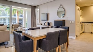 A modern hotel room with a dining area, a kitchen, and a balcony with palm trees. - Modern Waterfront Apartment w Canal Views Gulmarn 201 (Cape Town)