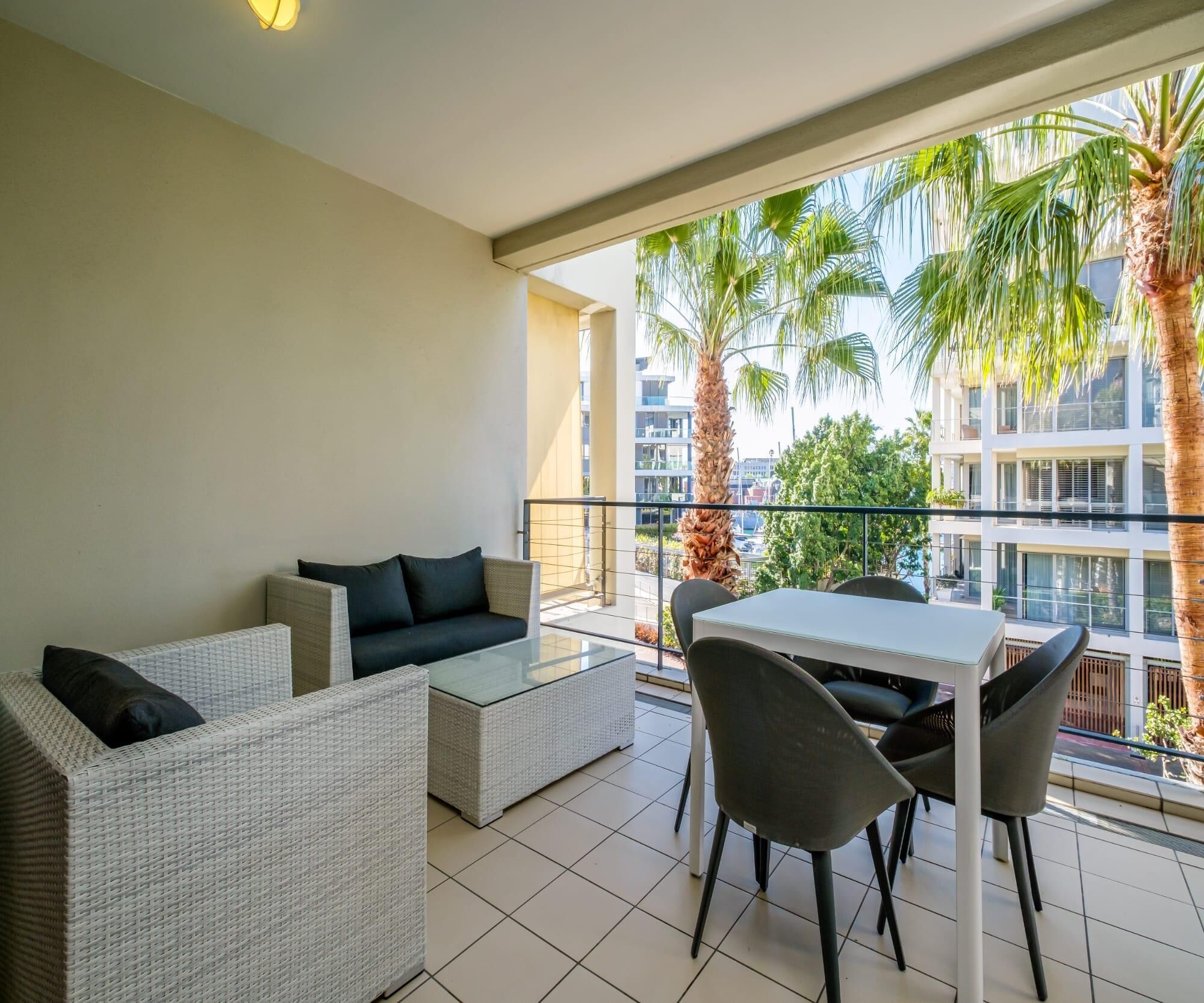 A balcony with wicker furniture, a glass table, and chairs.