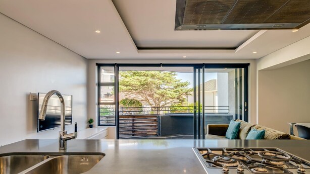 A modern kitchen with a stainless steel sink, a gas stove, and a large window overlooking a balcony. - Conveniently Located Apartment in Green Point C on S (Cape Town)