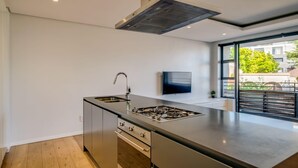 A modern kitchen with a stainless steel range hood, a built-in sink, and a flat-screen TV mounted on the wall. - Conveniently Located Apartment in Green Point C on S (Cape Town)