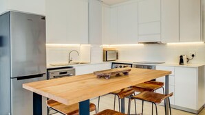 A modern kitchen with white cabinets, a stainless steel refrigerator, a microwave, and a wooden dining table with bar stools. - Gorgeous Apartment in Bustling De Waterkant 304 on N (Cape Town)
