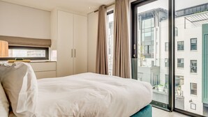 A modern bedroom with a large bed, a window with curtains, and a view of the city. - Gorgeous Apartment in Bustling De Waterkant 304 on N (Cape Town)