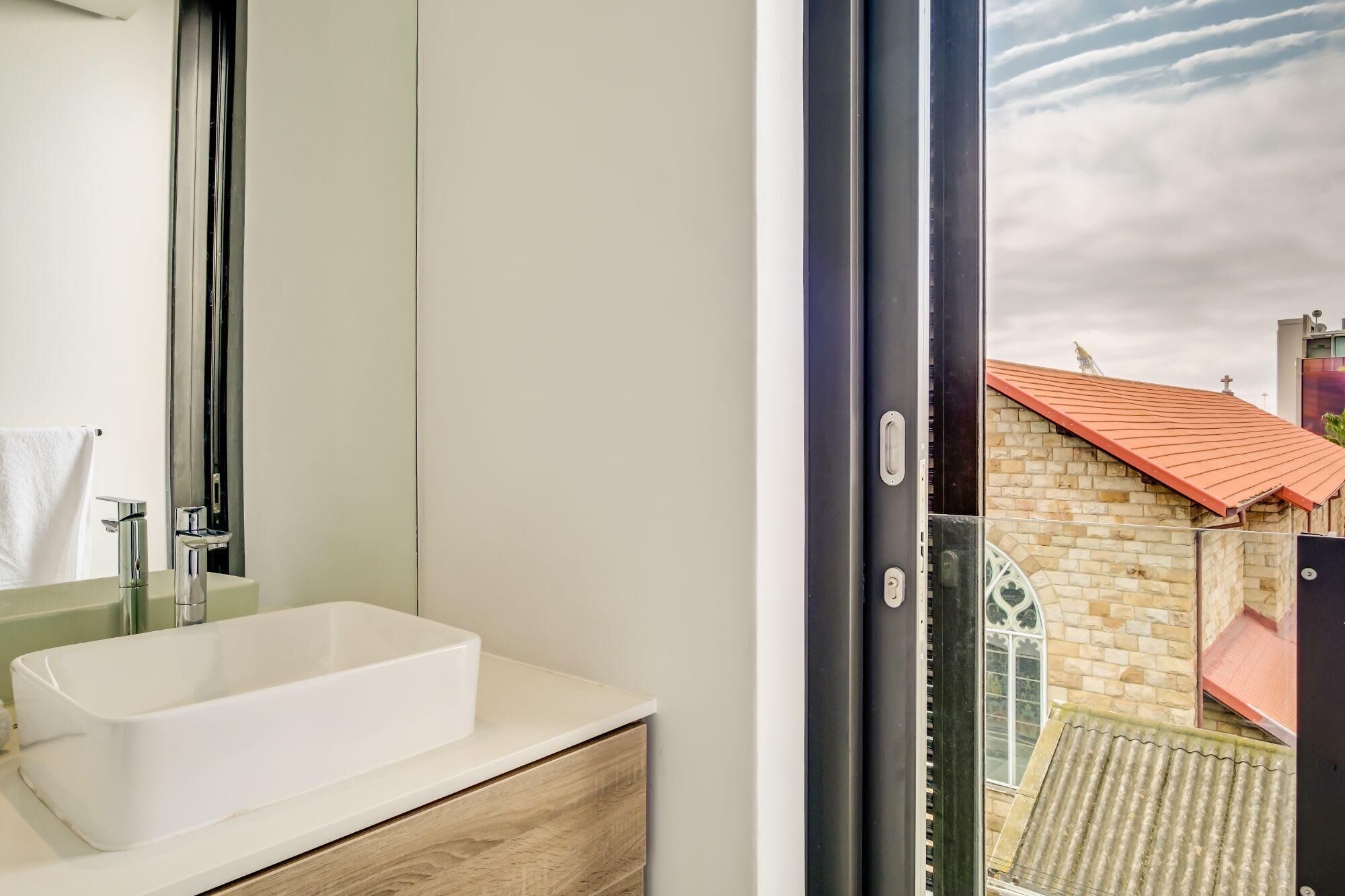 Een badkamer met een witte wastafel, een houten opbergmeubel en een grote spiegel.