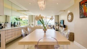A modern dining area with a long table, chairs, and a chandelier. - Elegant Apartment at the Waterclub Amani Views (Cape Town)
