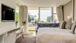 A hotel room with a large bed, a desk with a chair, a TV, and a balcony with curtains. - Elegant Apartment at the Waterclub Amani Views (Cape Town)