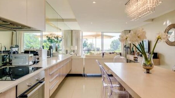 A modern kitchen with a central island, a chandelier, and a view of the outdoors. - Elegant Apartment at the Waterclub Amani Views (Cape Town)