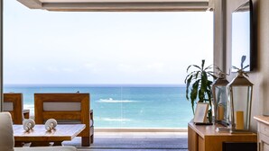 Quarto com vista para o oceano, uma mesa de madeira, cadeiras, uma planta e um abajur.