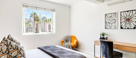Un dormitorio moderno con una cama grande, un escritorio, una silla y dos obras de arte en la pared.