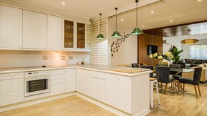 Une cuisine moderne avec des meubles blancs, un four encastré et un coin repas comprenant une table et des chaises en verre.