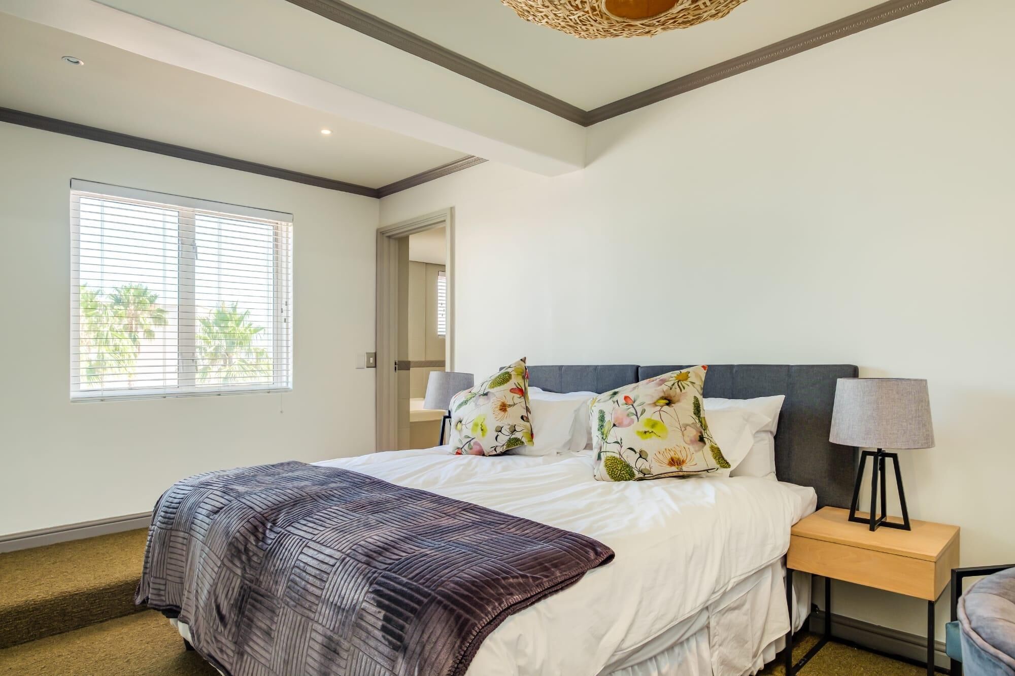 A bedroom with a bed, a nightstand, a lamp, and a window with blinds.