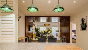 Un espace de salle à manger moderne avec une table et des chaises en bois, un grand vase rempli de fleurs et un luminaire suspendu vert.
