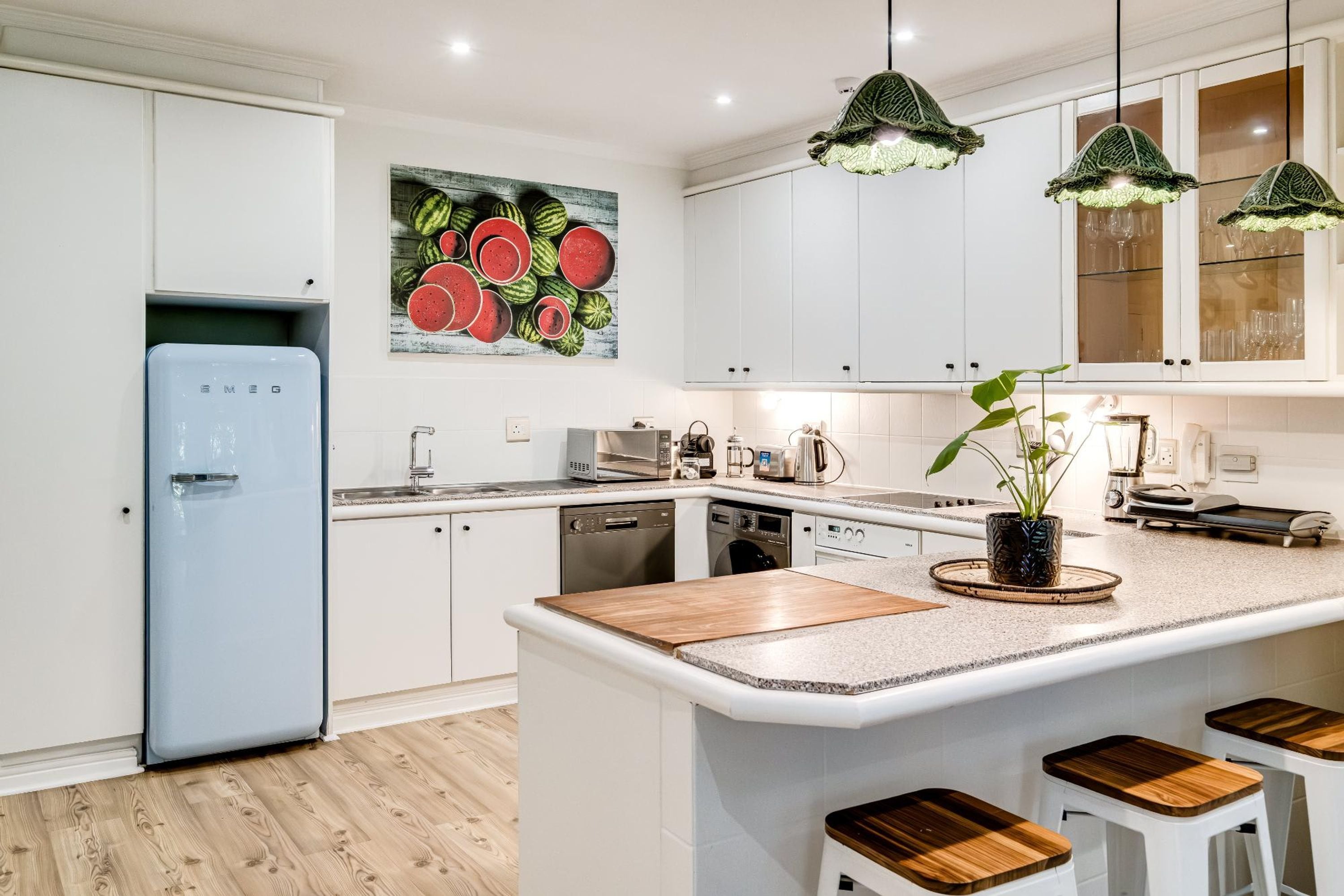 A modern kitchen with white cabinets, a blue refrigerator, a central island with stools, and pendant lighting.