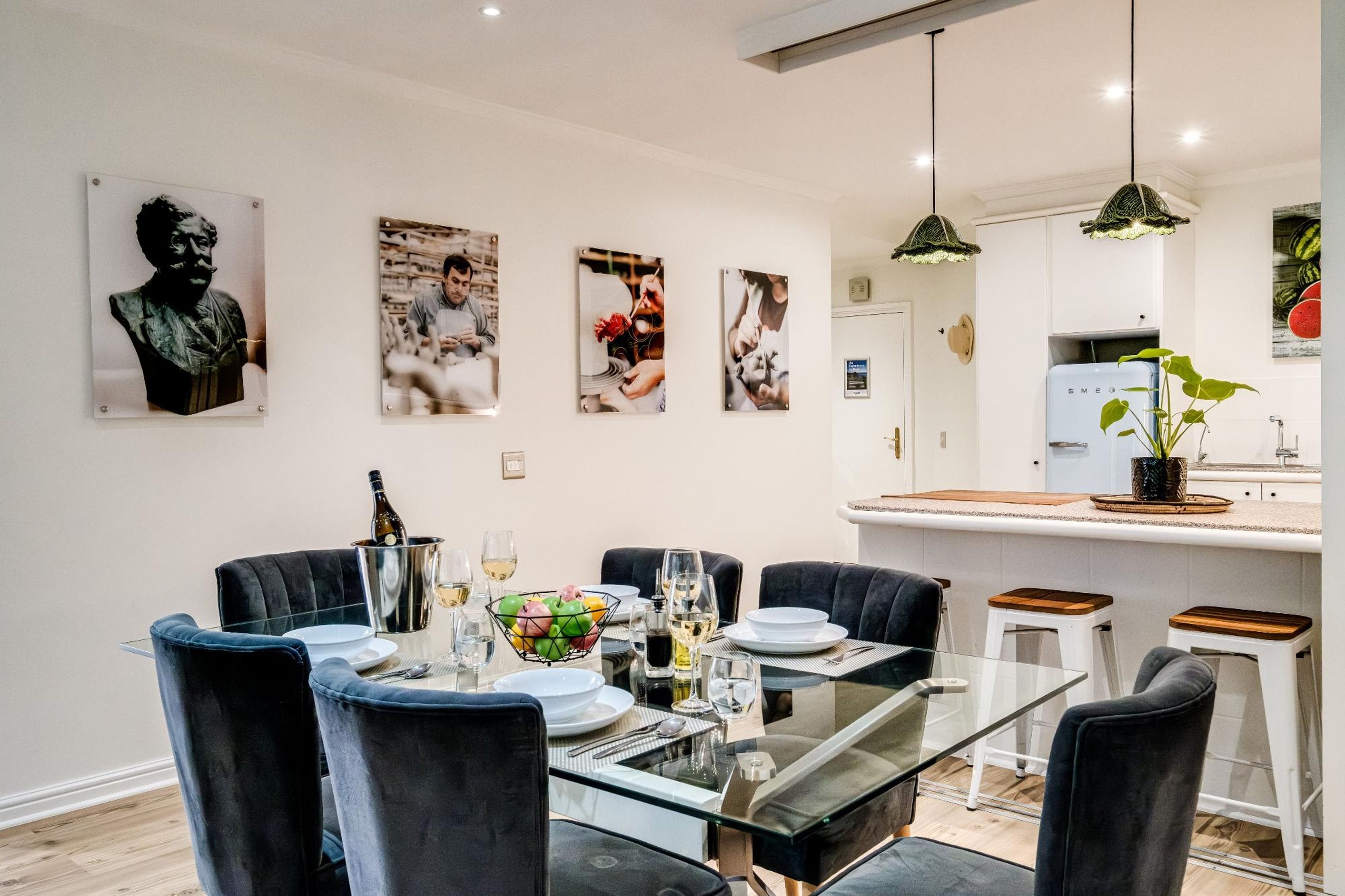 A modern dining area with a glass table, black chairs, and a white kitchen in the background.