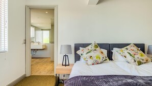 Une chambre à coucher avec un lit, deux oreillers, une table de chevet avec une lampe et une fenêtre avec des stores.