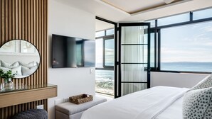 Une chambre moderne avec un grand lit, un téléviseur fixé au mur, un mur recouvert de panneaux en bois et une vue sur l’océan.