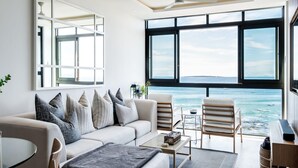 Un salon moderne doté d’une grande fenêtre donnant sur la mer, d’un ventilateur de plafond et d’un design minimaliste.