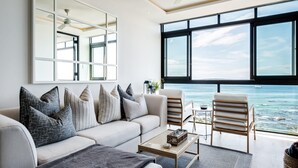 Un salon moderne doté d’une grande fenêtre donnant sur la mer, d’un ventilateur de plafond et d’un canapé agrémenté de coussins à motifs.