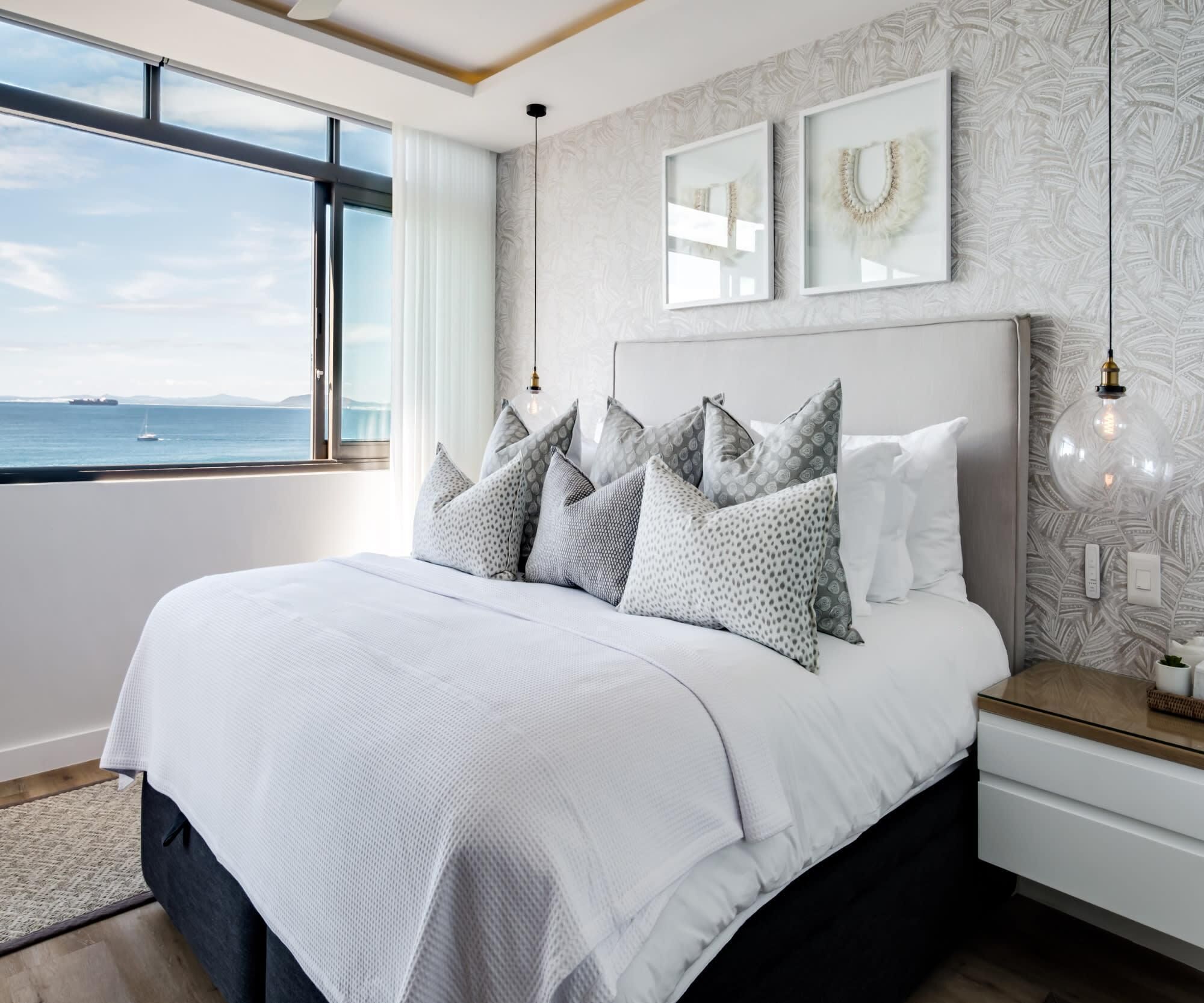 Une chambre moderne avec un grand lit, une vue sur la mer et un mur décoré de motifs.
