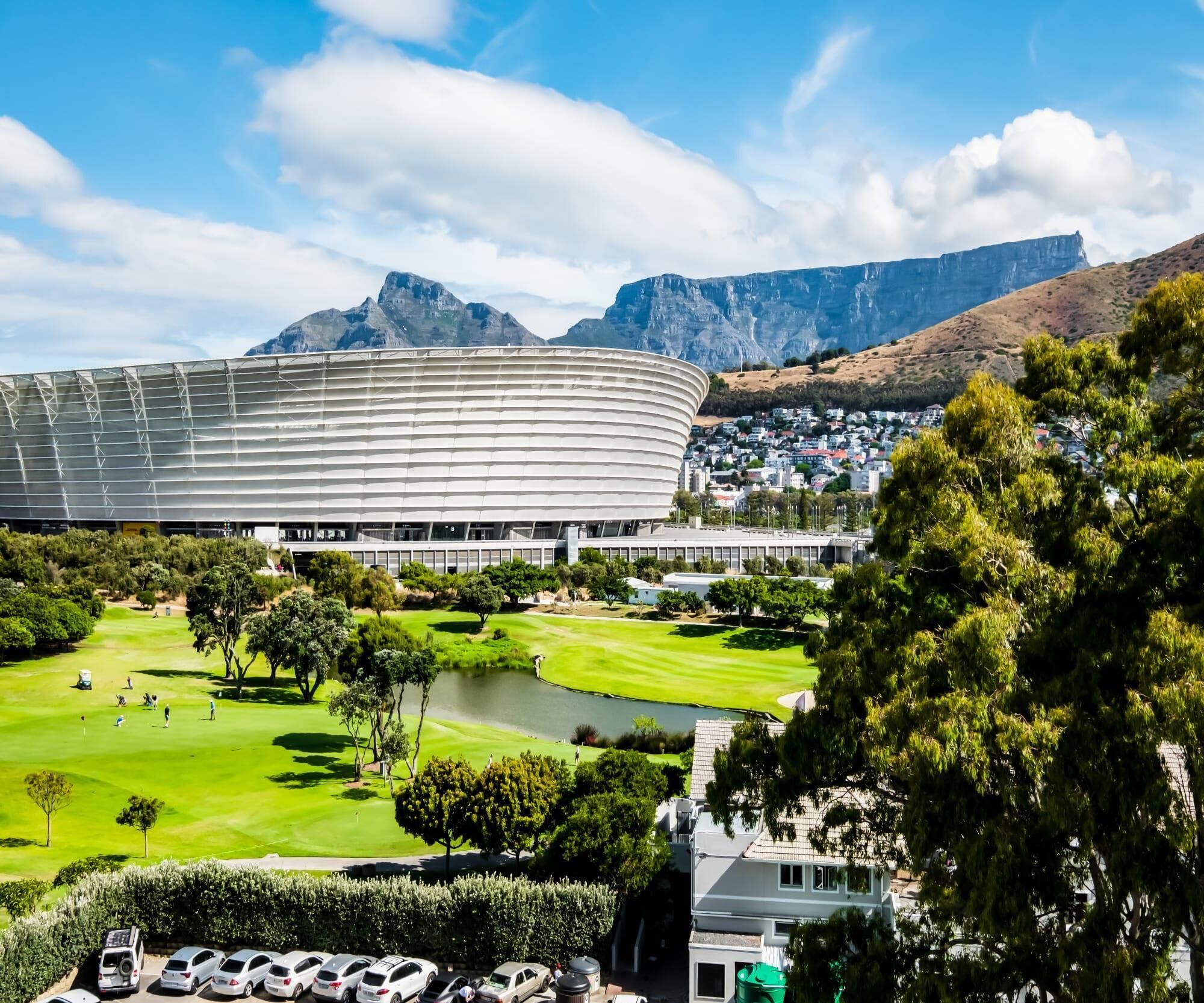 A large stadium with a curved roof, surrounded by a golf course and residential buildings.