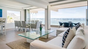 Ein modernes Wohnzimmer mit Glastisch, weißem Sofa und Essbereich mit Stühlen.