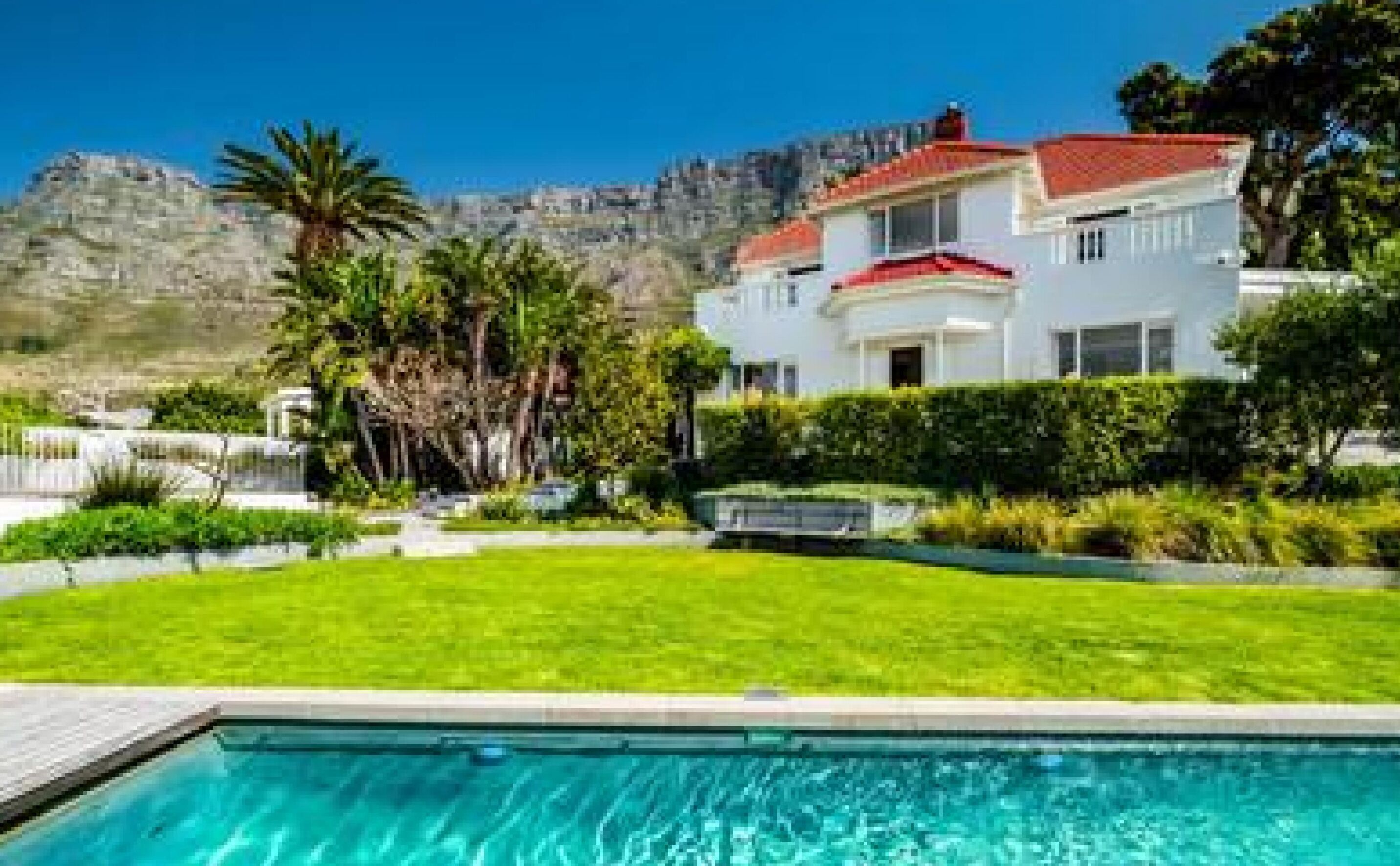 A two-story house with a red roof, surrounded by a well-maintained lawn and a swimming pool.