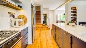 A modern kitchen with a gas stove, wooden flooring, and a staircase leading to a living area. - Magnificent Heritage Home w Sweeping Views of the City Oranjezicht Heritage (Cape Town)