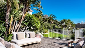A wooden deck with outdoor furniture, surrounded by lush greenery and a view of a residential area. - Magnificent Heritage Home w Sweeping Views of the City Oranjezicht Heritage (Cape Town)