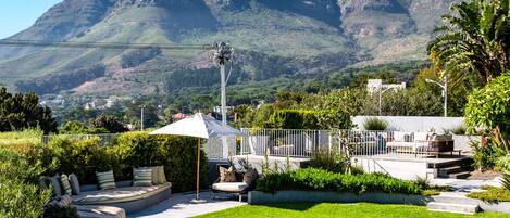 A pool area with a seating arrangement, surrounded by greenery and a view of a mountain.