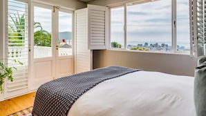 A bedroom with a bed, a view of a cityscape, and a balcony with plants. - Magnificent Heritage Home w Sweeping Views of the City Oranjezicht Heritage (Cape Town)