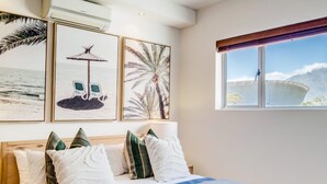 A bedroom with a bed, pillows, a nightstand, and wall art depicting beach scenes. - Uninterrupted Ocean Views in Mouille Point Atlantic Vistas (Cape Town)