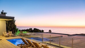 A wooden deck with a pool and lounge chairs overlooking the ocean at sunset. - Perfect Family Holiday Villa in Camps Bay Spindrift (Cape Town)