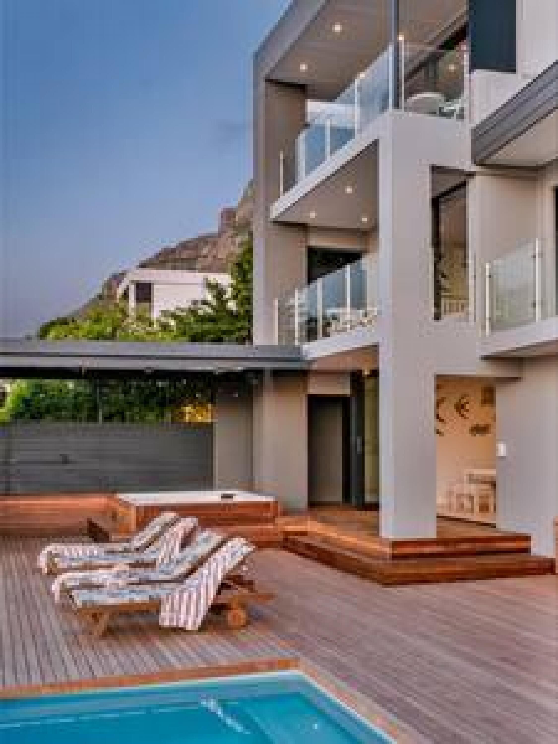 A modern multi-story building with a rooftop pool area, including lounge chairs and a wooden deck.
